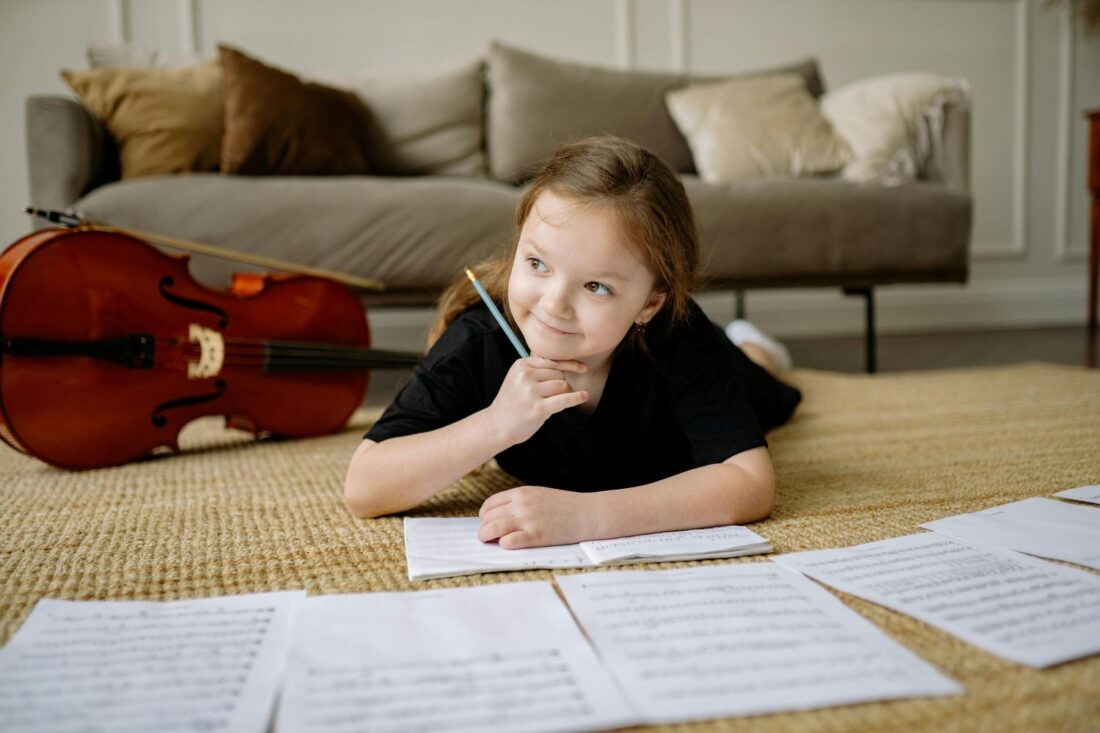 Girl lying on the floor writing in a book with a 'cello in the background