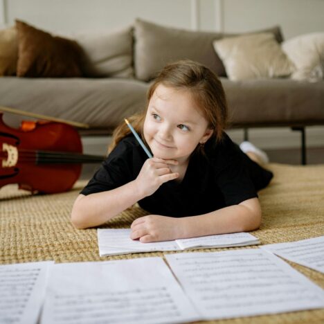 Girl lying on the floor writing in a book with a 'cello in the background